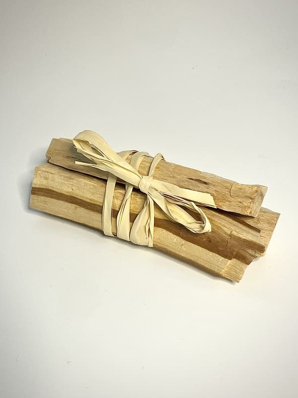 3 bâtons de Palo Santo relié ensemble par du radia avec noeud apparent sur fond banc
